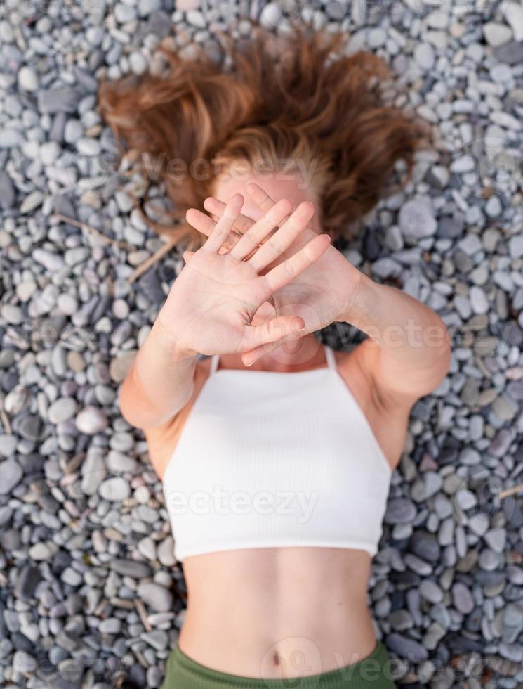 giovane donna sorridente sdraiata sulla spiaggia di pietra, che copre il viso con le mani foto