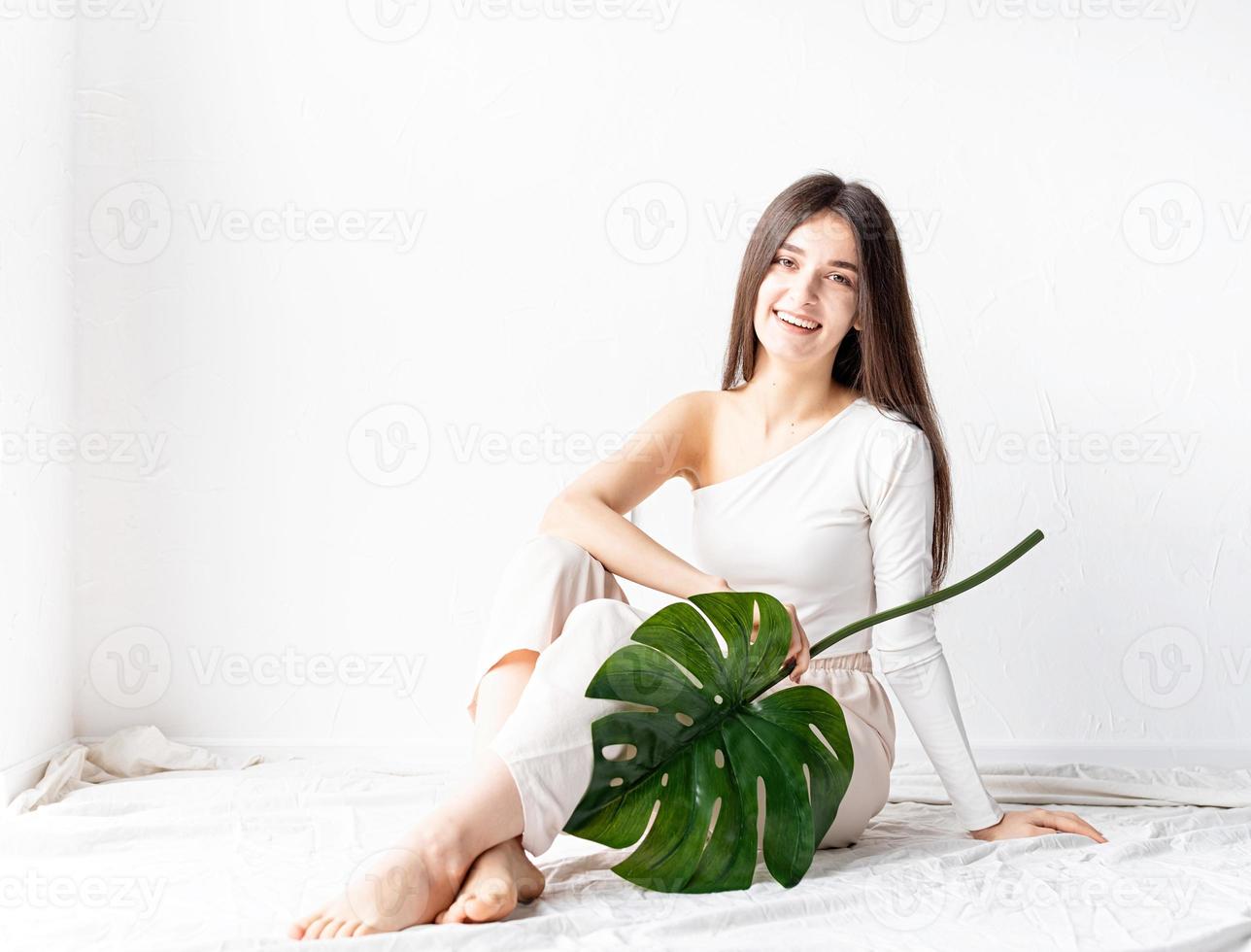 bella donna felice in abiti comodi che tiene una foglia verde di monstera green foto