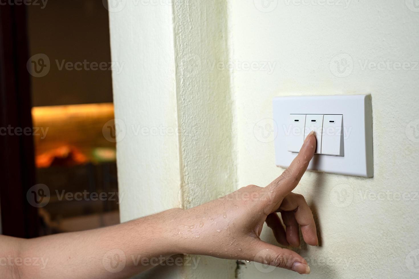 la mano bagnata accende le luci interruttore elettrico sullo sfondo del muro bianco foto