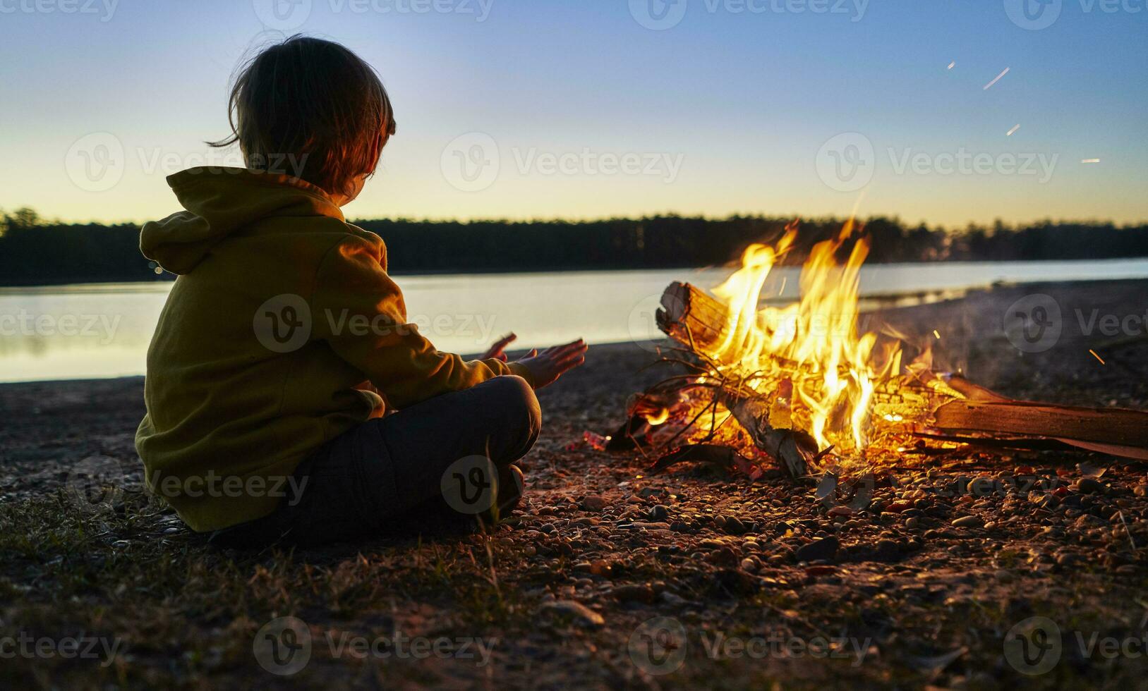 argentina, patagonia, concordia, ragazzo seduta a campo fuoco a un' lago foto