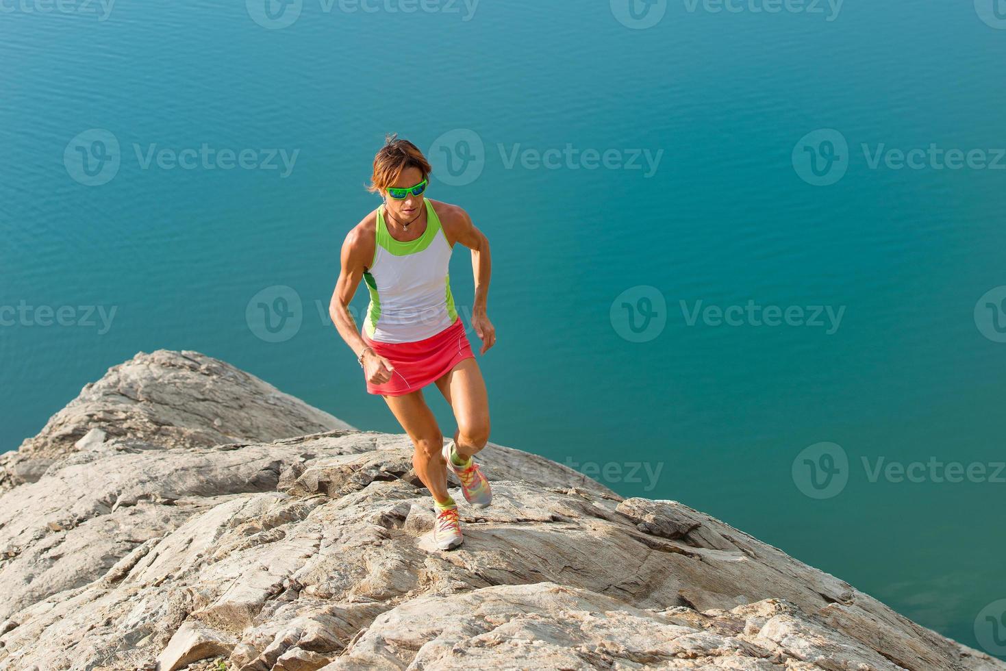 la ragazza skyrunner corre su un dorso sassoso sopra un lago foto