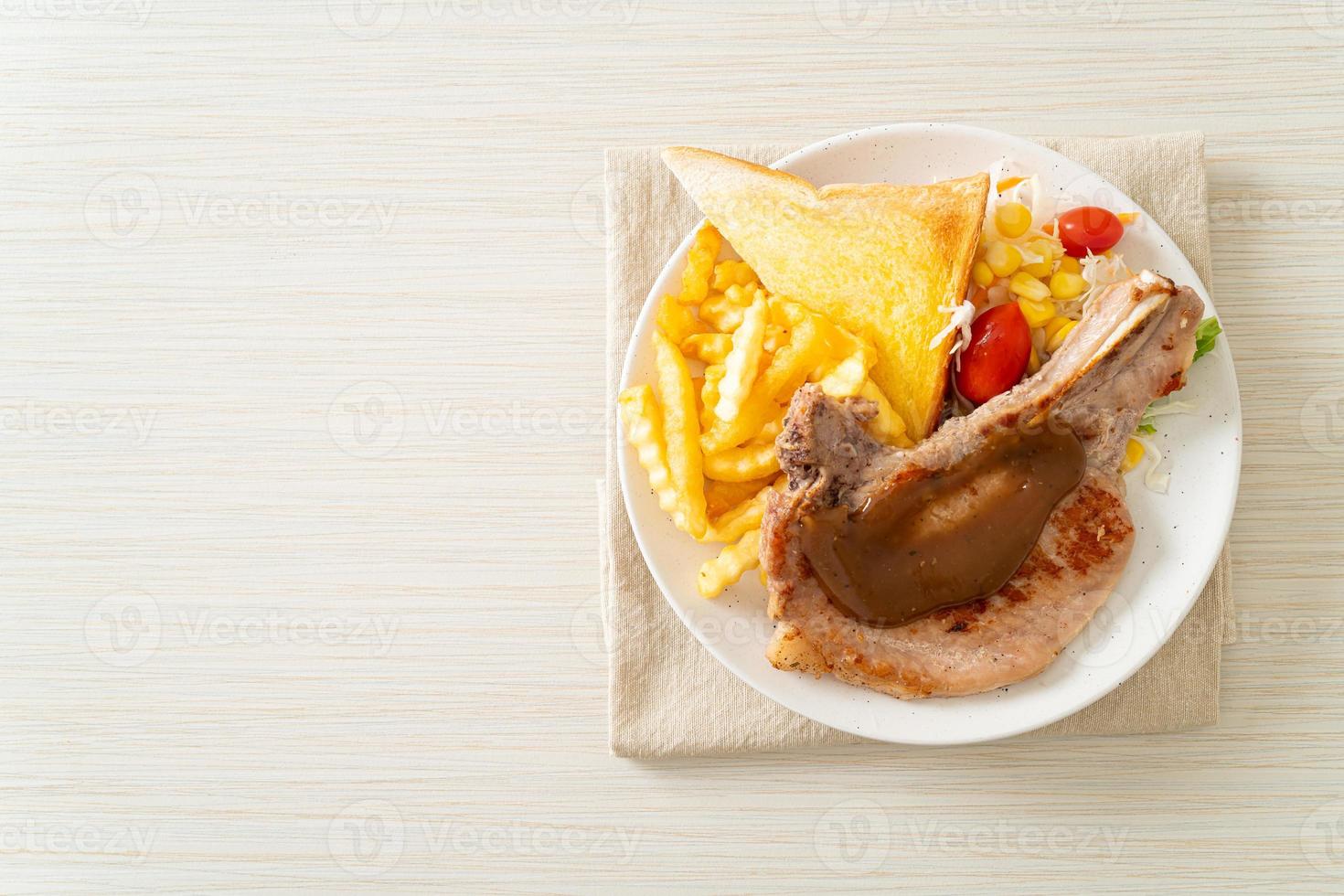 bistecca di braciola di maiale con patatine e mini insalata su piatto bianco foto