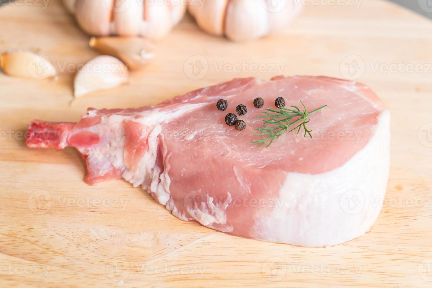 braciola di maiale fresca su tavola di legno con aglio e peperoni neri foto