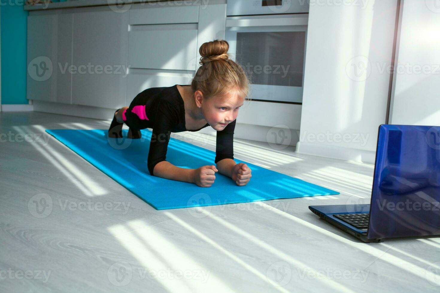 poco ragazza fare yoga tavola e Guardando in linea Lezioni su computer portatile, esercizio nel il cucina. foto