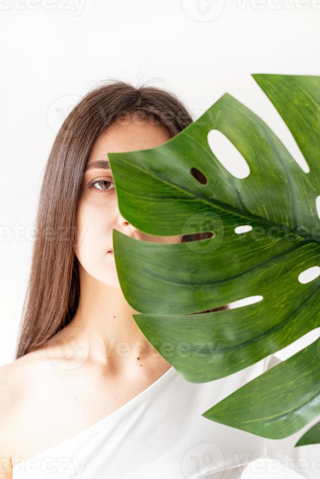 donna che tiene una foglia di monstera verde davanti al viso foto