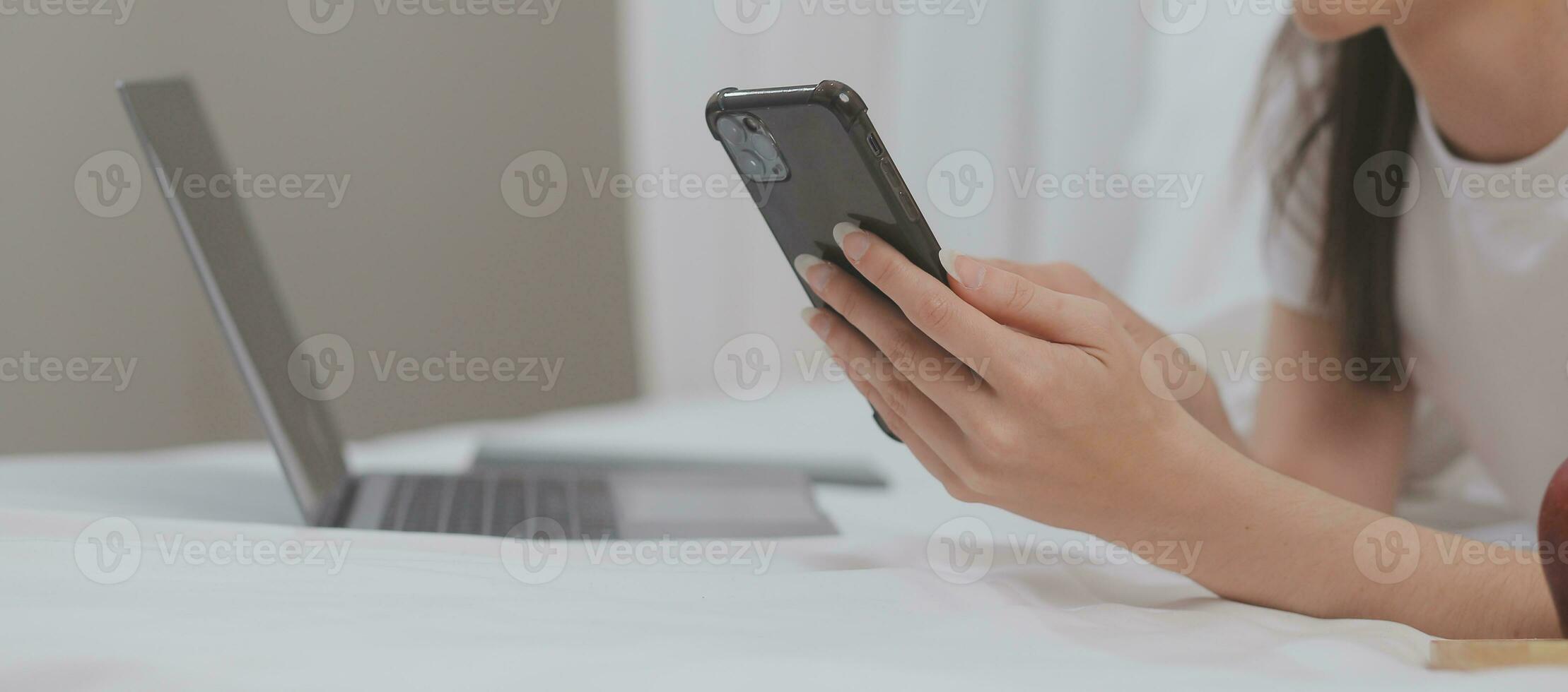 efficiente giovane del Millennio ragazza seduta su un' letto nel il mattina, usi il computer portatile computer e mangia Cornetti e bevande caffè per prima colazione foto