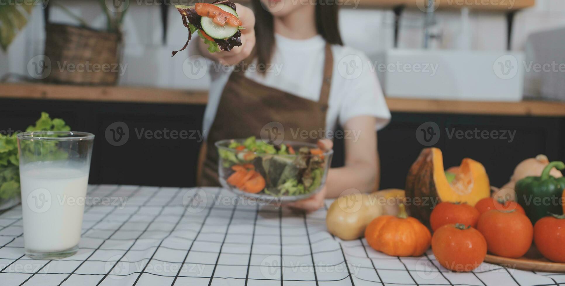 delizioso frutta e verdure su un' tavolo e donna cucinando. casalinga è taglio verde cetrioli su un' di legno tavola per fabbricazione fresco insalata nel il cucina. foto