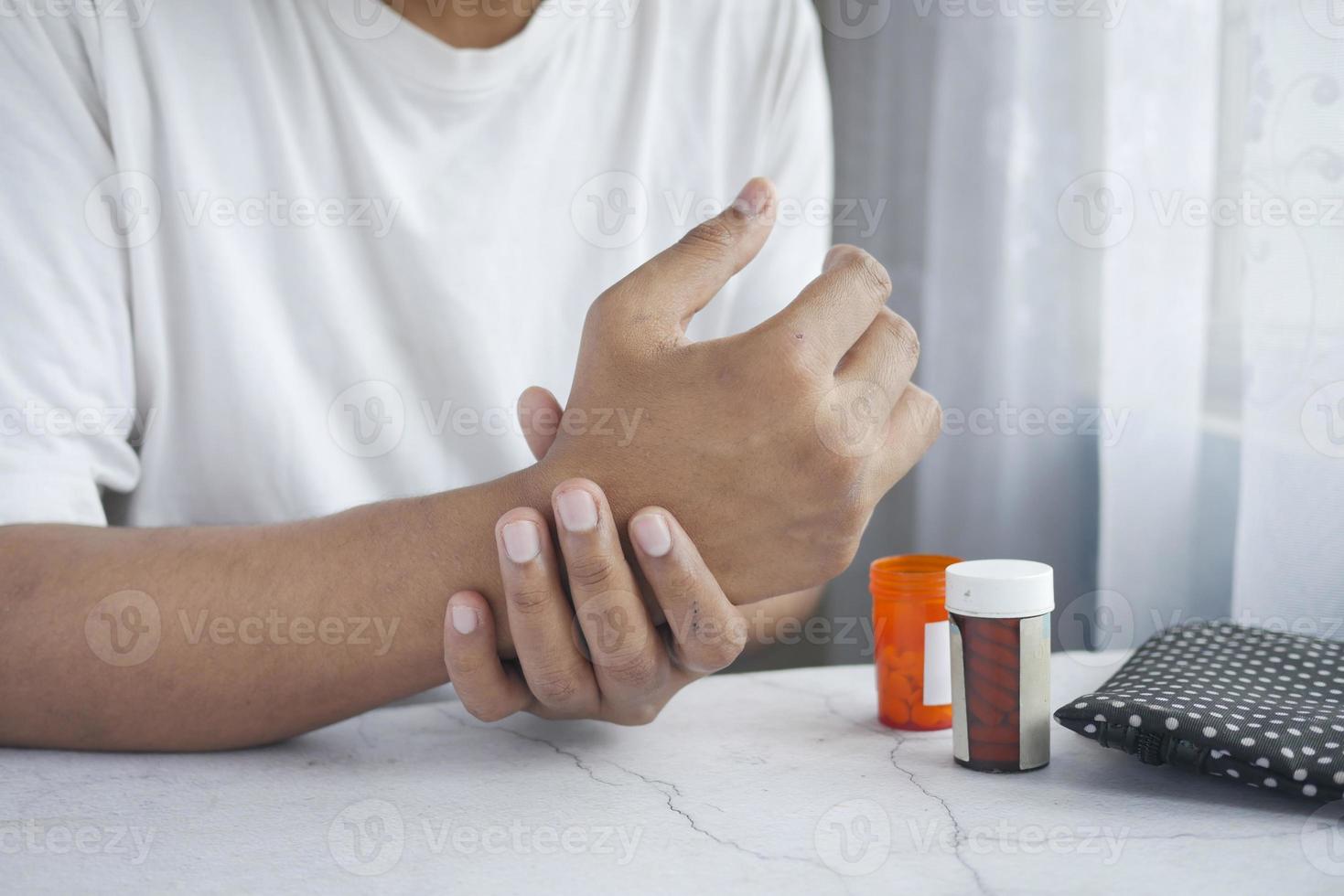 uomo che soffre di dolore alla mano e pillole mediche sul tavolo foto