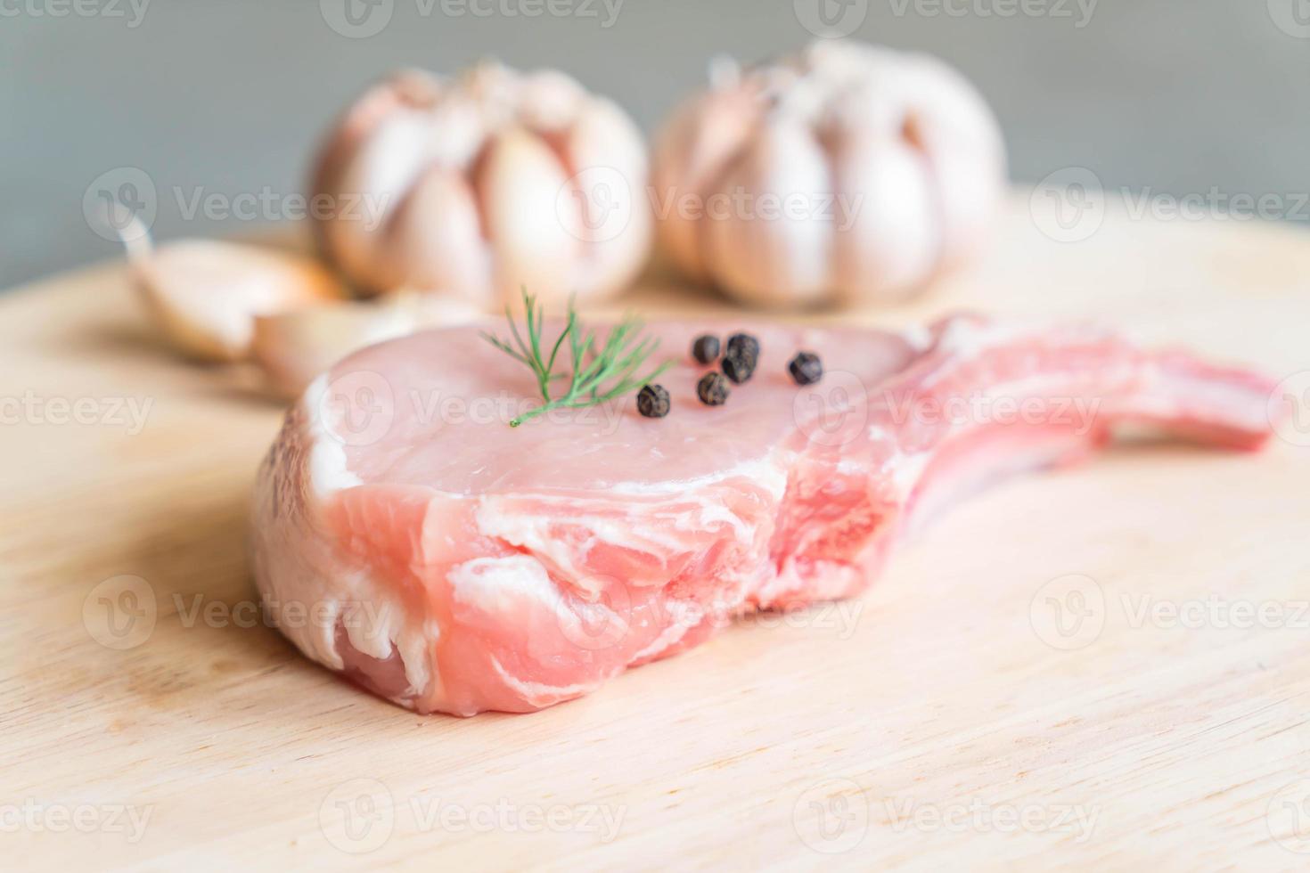 braciola di maiale fresca su tavola di legno con aglio e peperoni neri foto