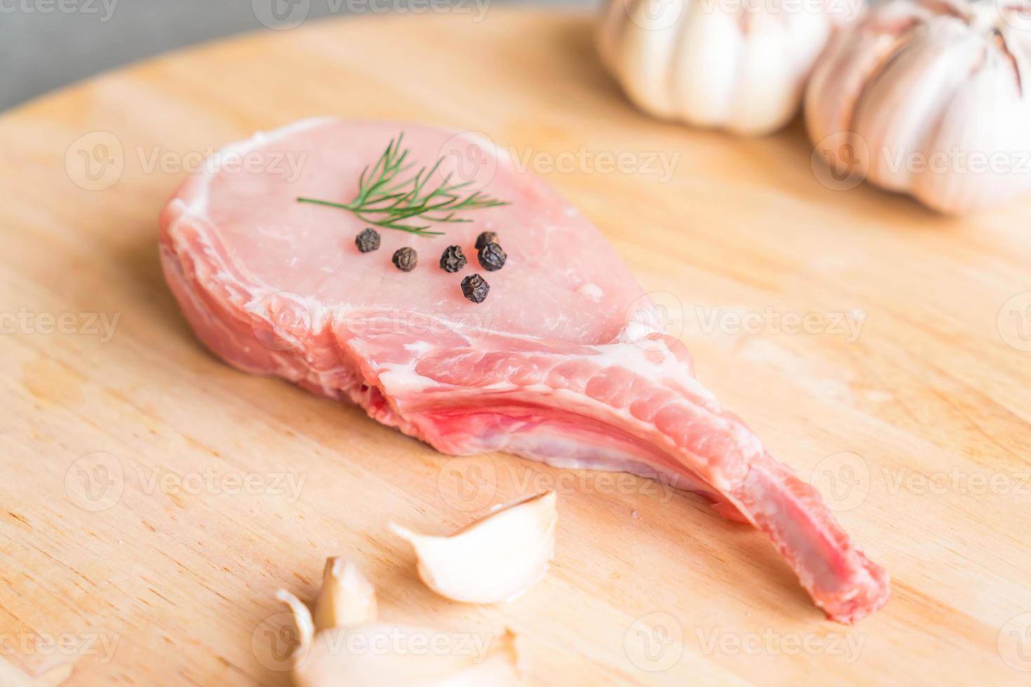 braciola di maiale fresca su tavola di legno con aglio e peperoni neri foto