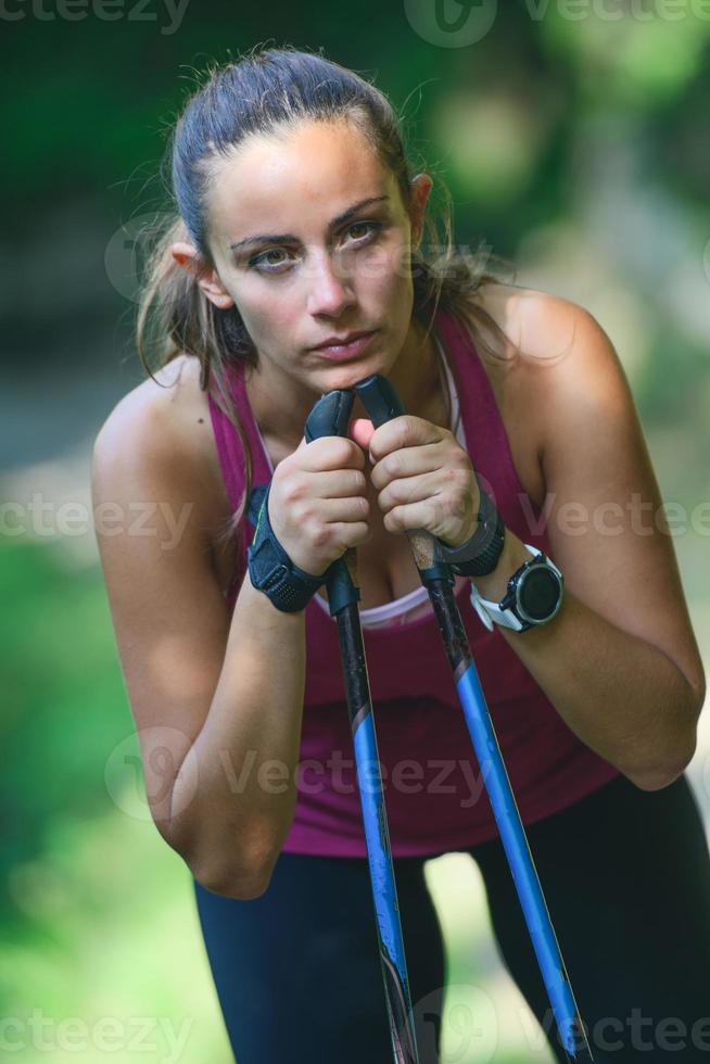 la giovane donna sportiva con i bastoncini da nordic walking sta riposando foto