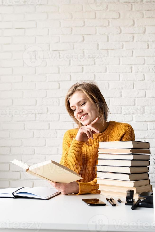 giovane donna sorridente in maglione giallo che legge un libro e ride foto