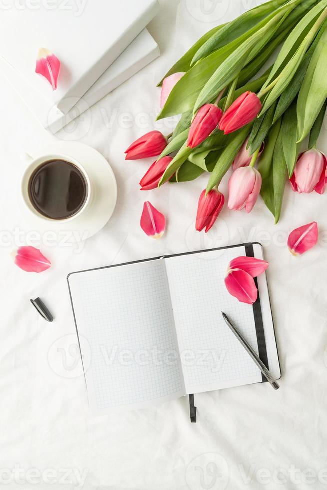 quaderno bianco aperto con tulipani e tazza di caffè sul letto bianco foto