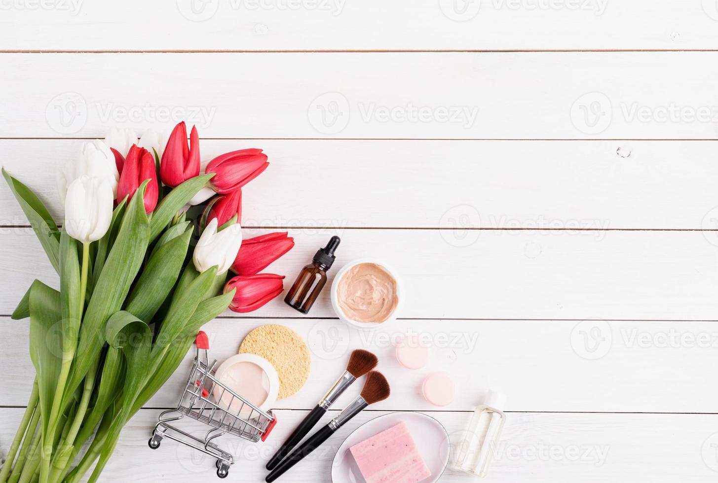 cosmetici con tulipani rosa distesi su fondo di legno bianco foto