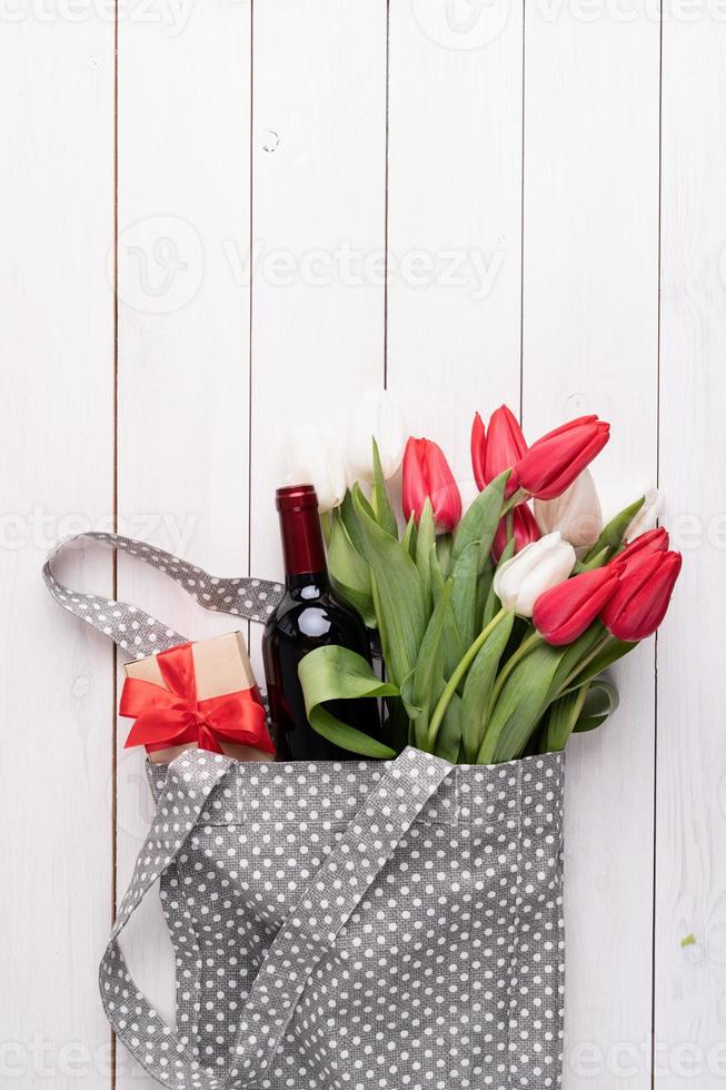 borsa in tessuto grigio piena di tulipani colorati e bottiglia di vino foto
