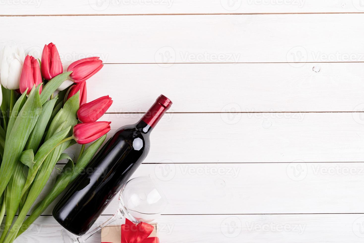 mazzo di tulipani colorati e bottiglia di vino su fondo di legno bianco foto