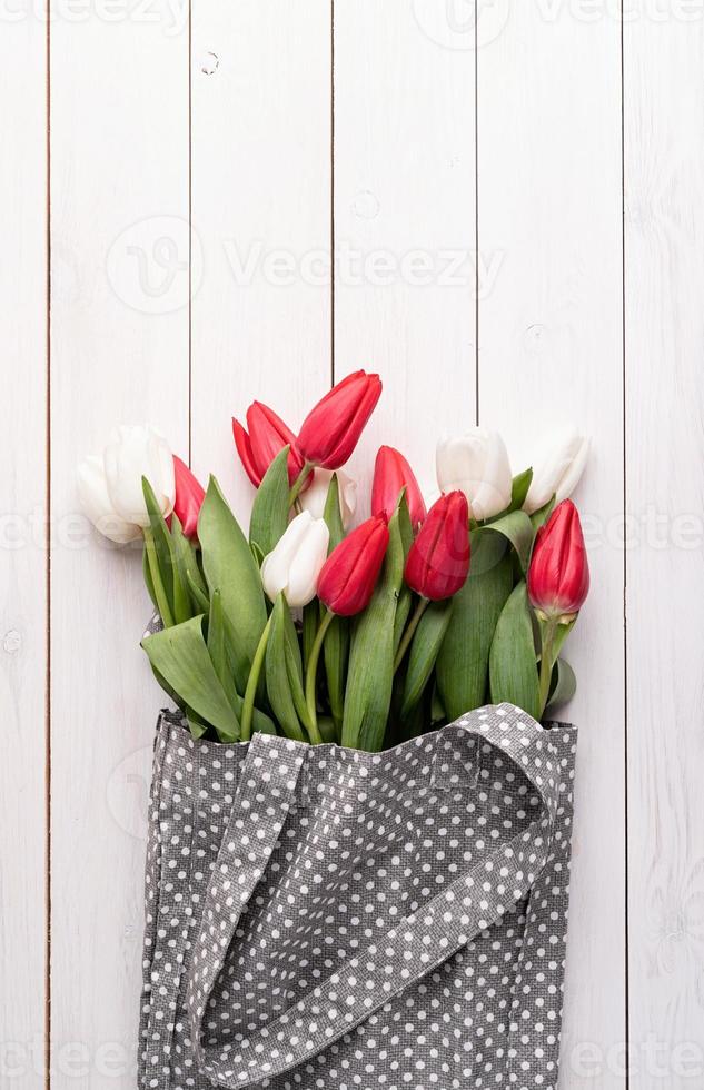 borsa in tessuto grigio piena di tulipani colorati su fondo in legno bianco foto