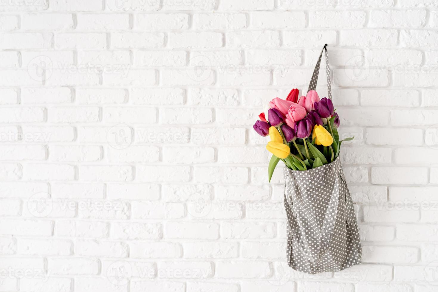 borsa in tessuto grigio piena di tulipani colorati su sfondo bianco mattone foto