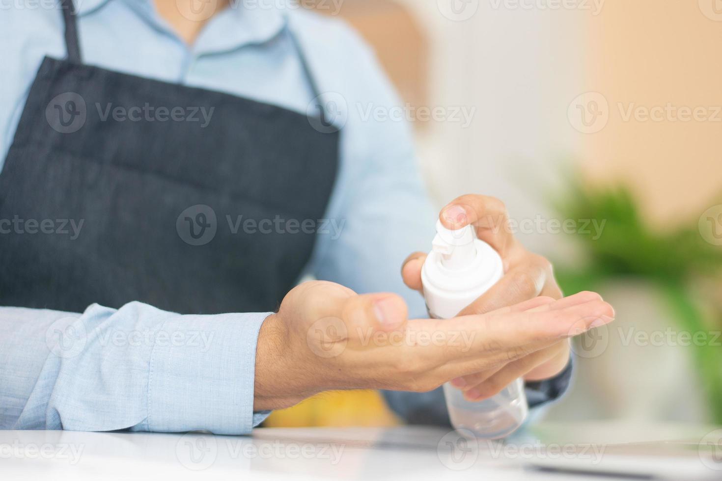 dipendente che usa la mano per la pulizia del gel alcolico per lavorare nella caffetteria foto