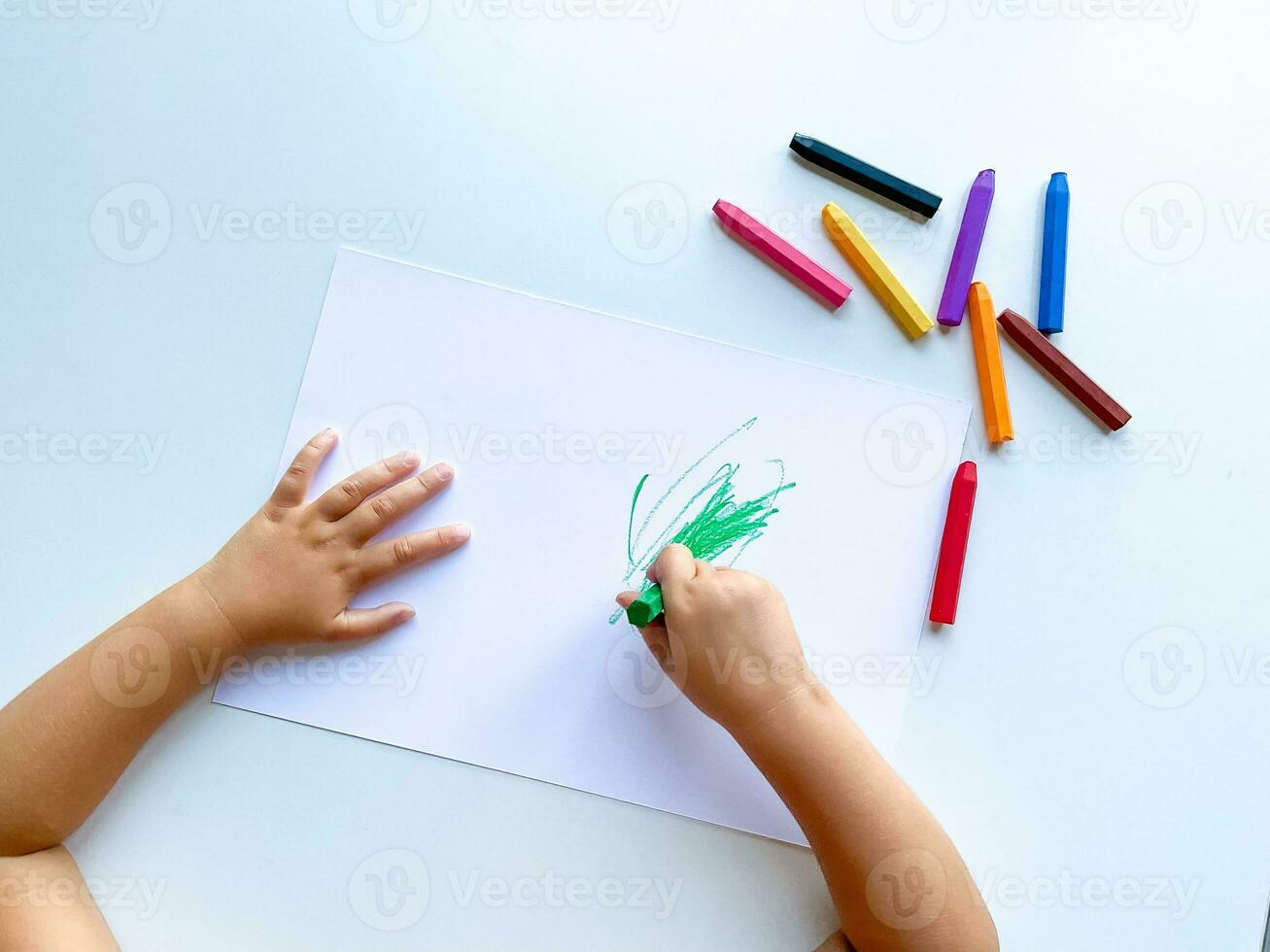 piccolo bambino disegna con pastello pastelli su bianca tavolo. foto