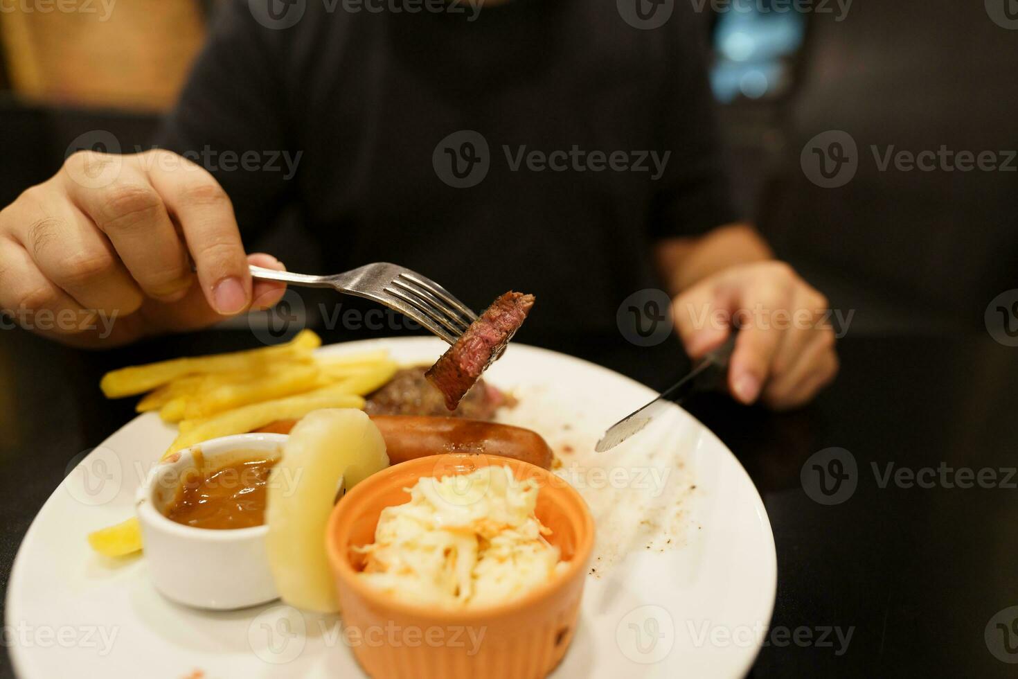 uomo mangiare grigliato carni palo a partire dal piatto. mano Tenere coltello e forchetta taglio grigliato Manzo bistecca foto
