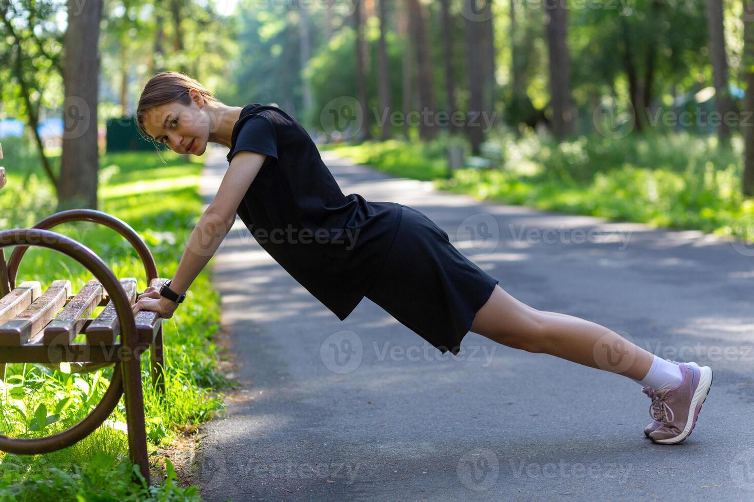 bellissimo giovane sportivo donna nel nero maglietta, nero pantaloncini e rosa formatori riscaldamento su esercizio tricipiti e il petto foto