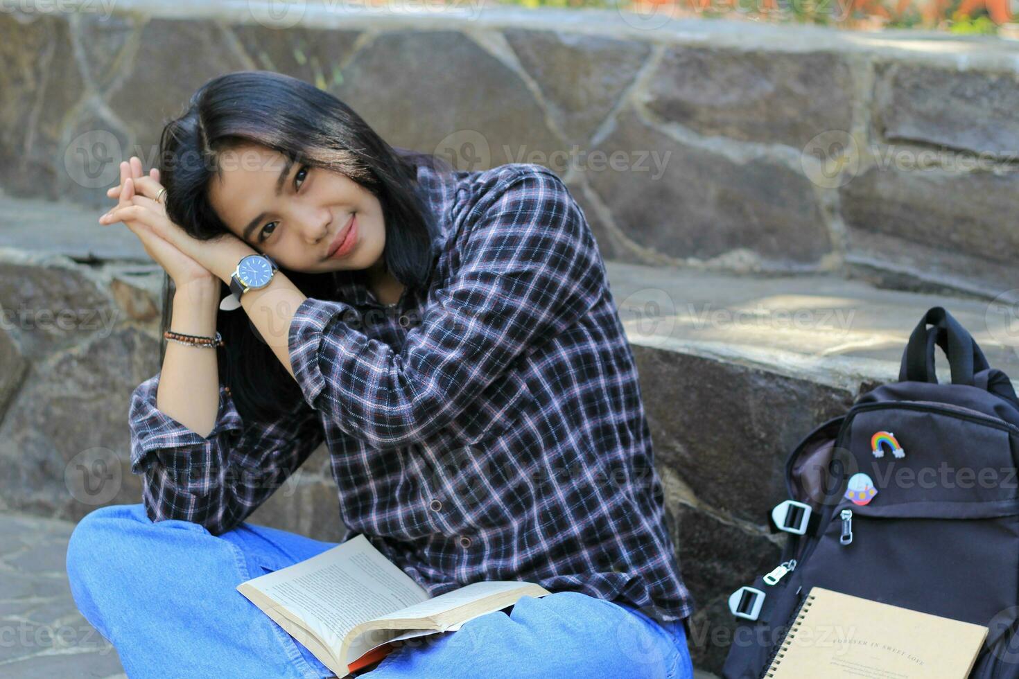 contento giovane asiatico donna Università alunno con sorridente viso godere leggere un' libro per esame nel il parco foto