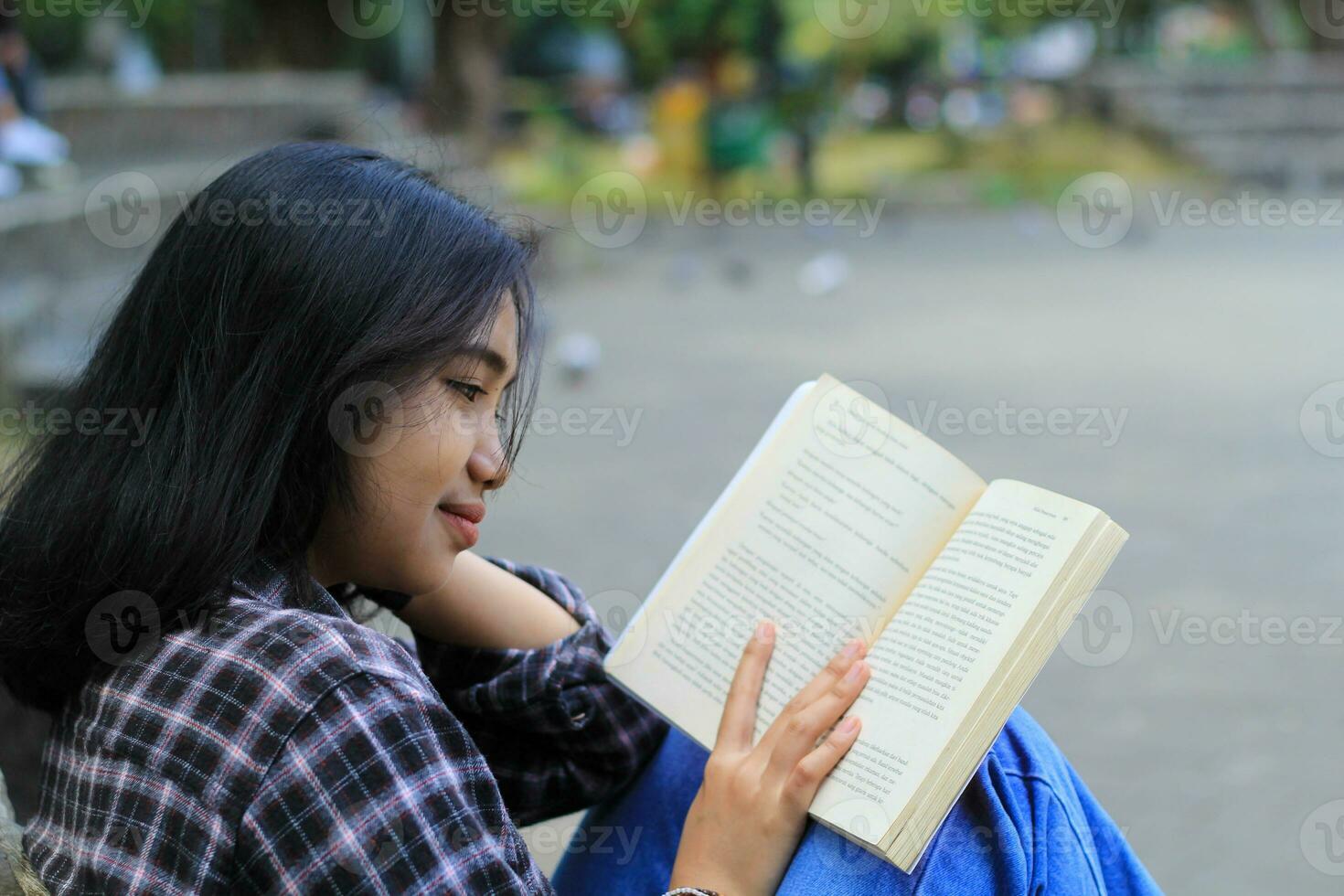 contento e succes femmina asiatico Università alunno godendo leggere un' libro nel il parco foto