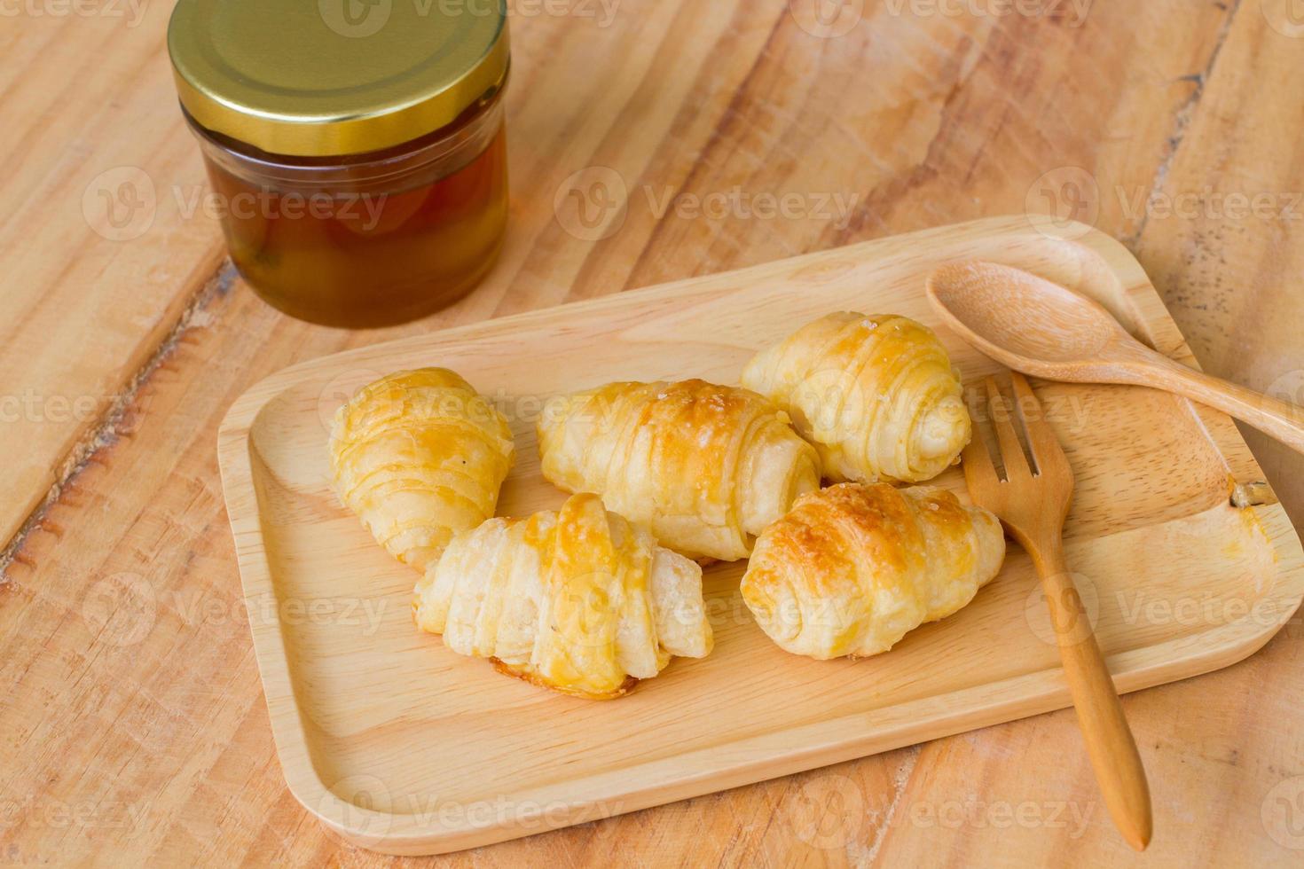 piccoli gustosi croissant sul piatto di legno vicino a cucchiaio e forchetta foto