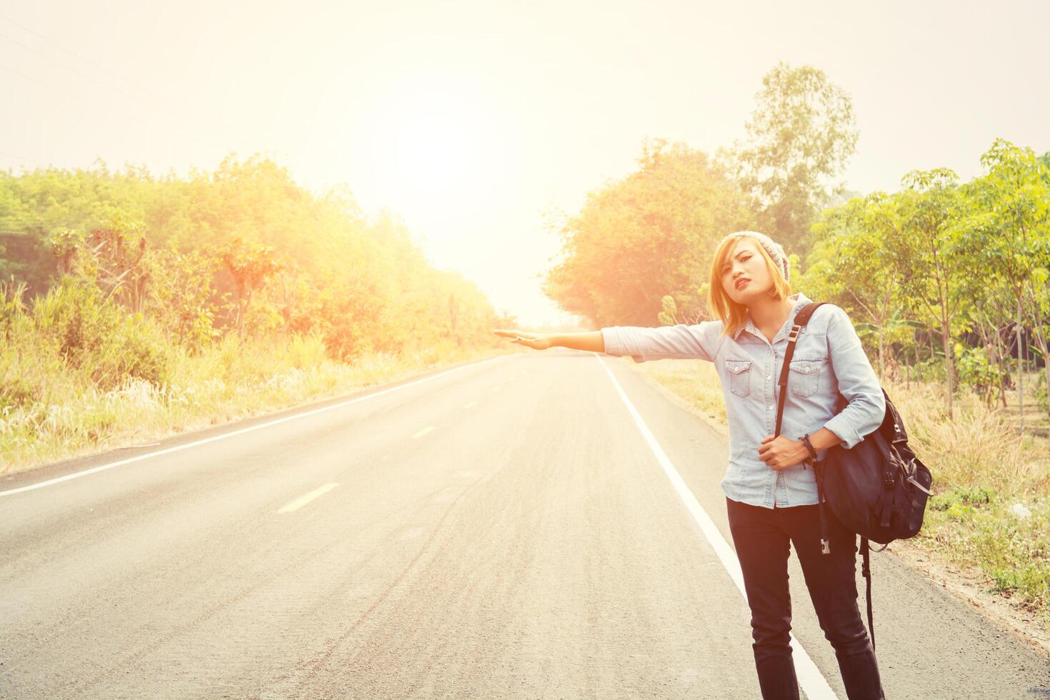 giovane donna hipster che fa l'autostop su una strada di campagna foto