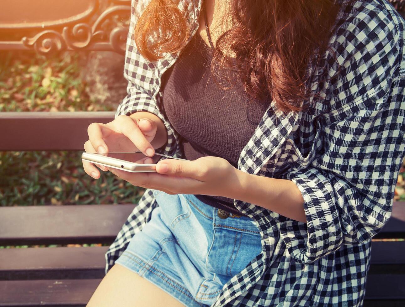 giovane donna che tiene il telefono cellulare che gioca seduto al parco. foto