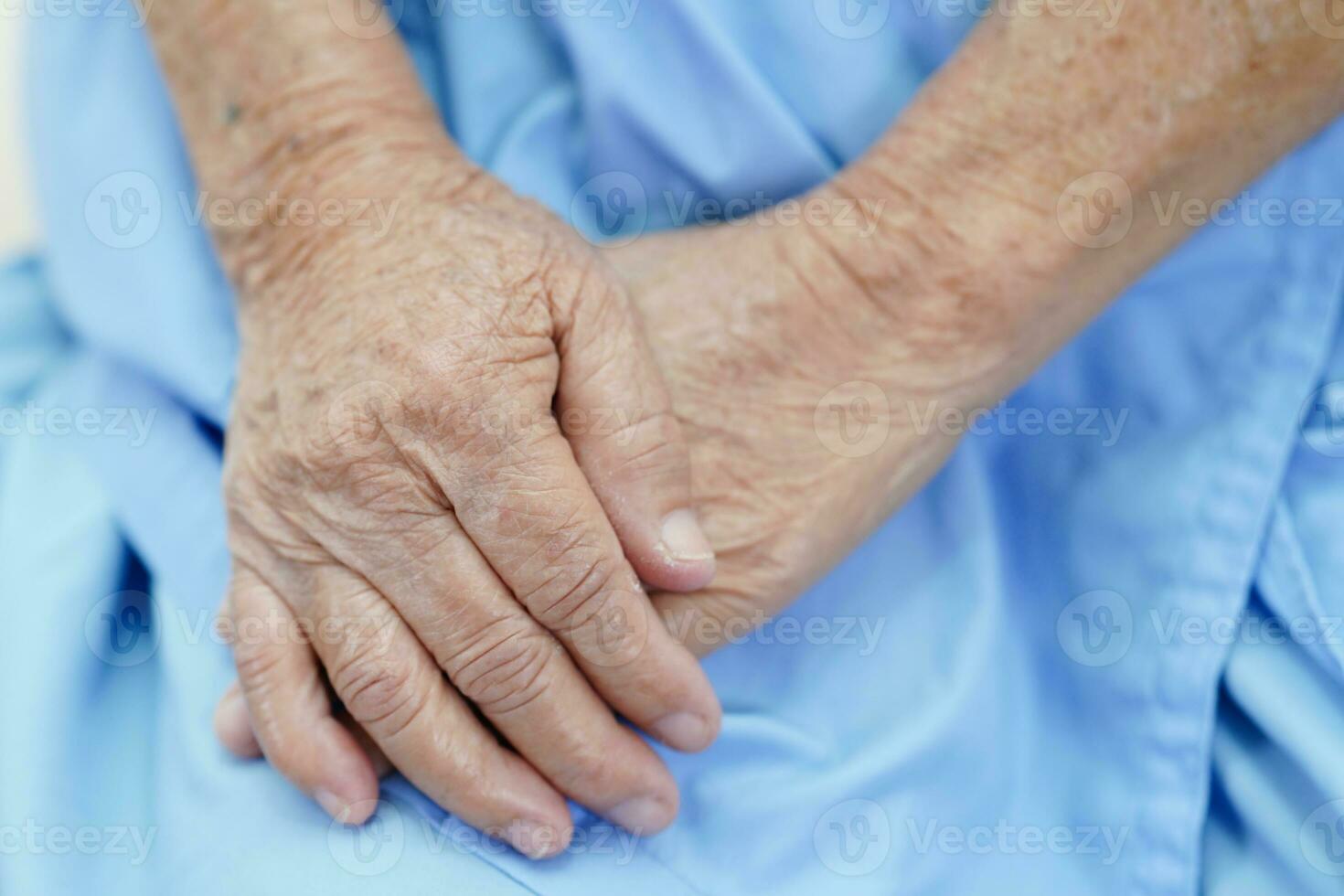 paziente anziano asiatico della donna che si siede sul letto in ospedale, primo piano alla sua mano. foto