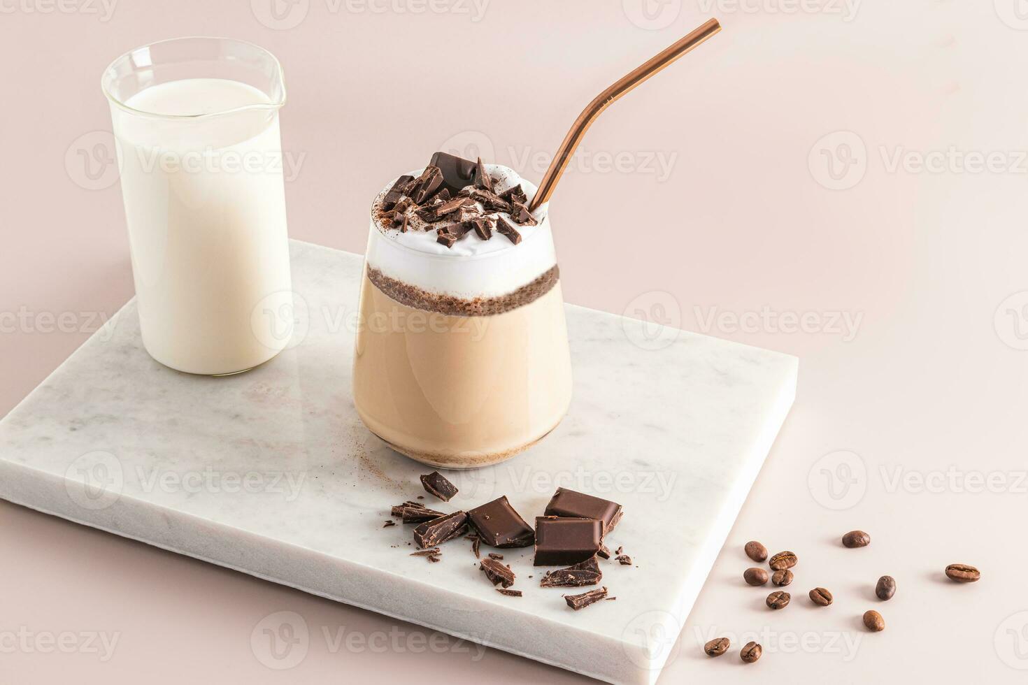 un' grande bicchiere con un' cioccolato bevanda e cioccolato cunei, un' latte macchiato con schiuma su un' marmo bianca podio con un' brocca di latte. il Perfetto dolce. foto