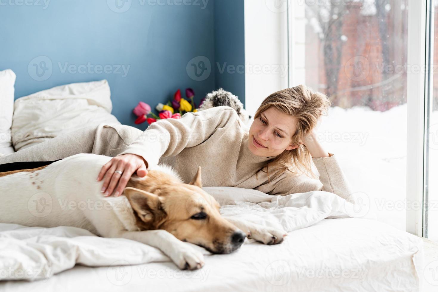 felice giovane donna sdraiata a letto con i suoi cani foto