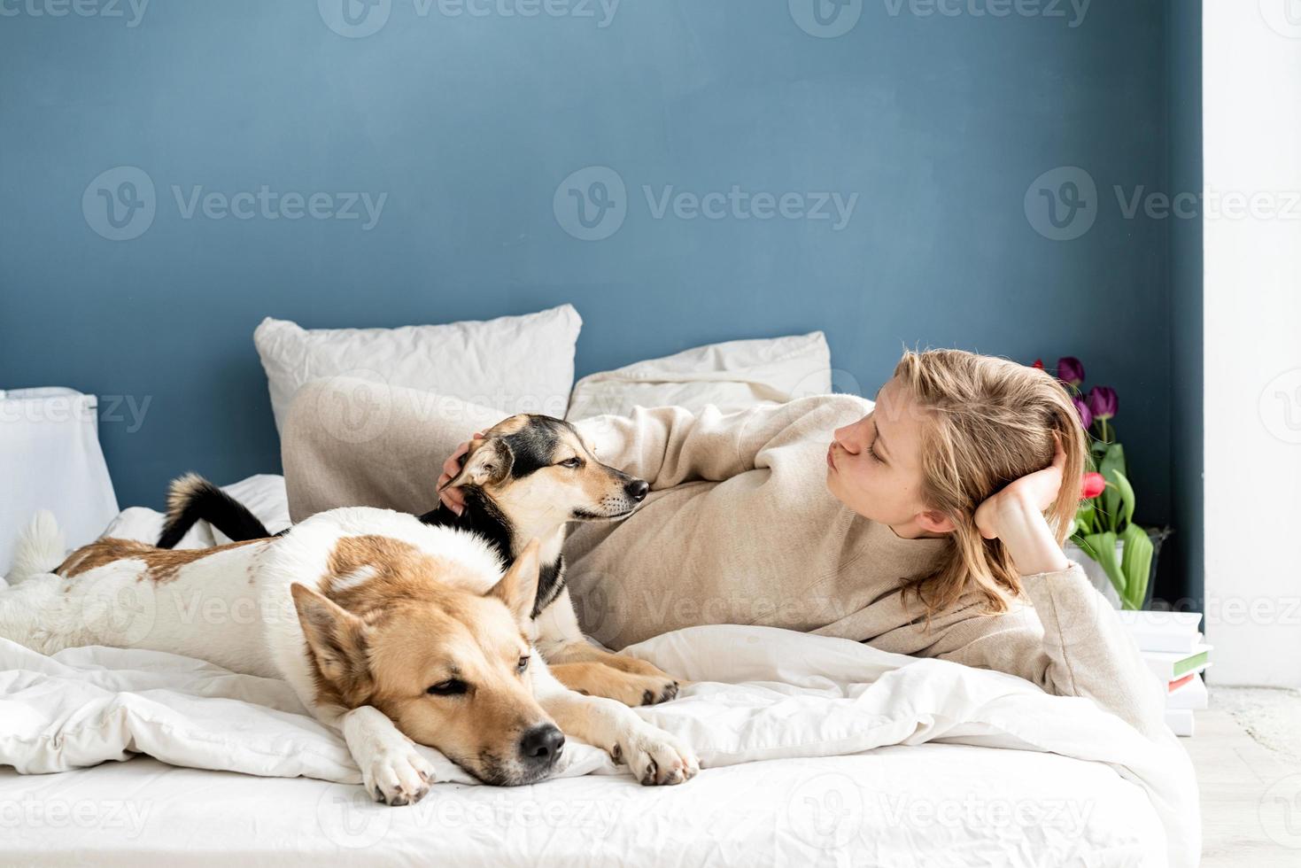 felice giovane donna sdraiata a letto con i suoi cani foto