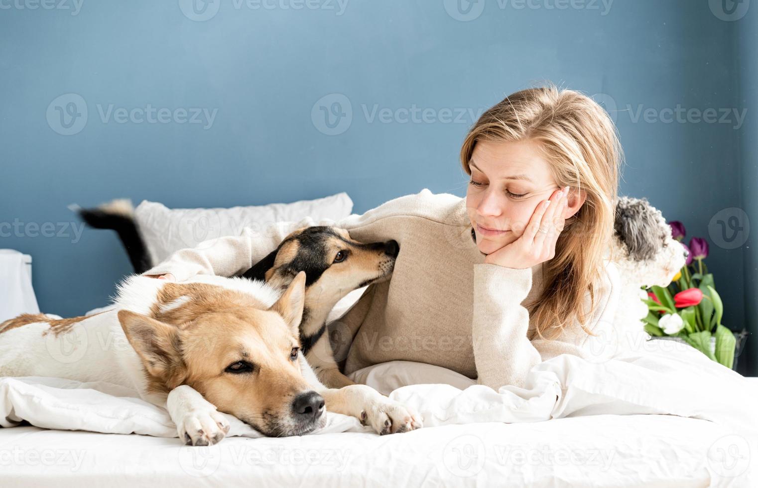 felice giovane donna sdraiata a letto con i suoi cani foto