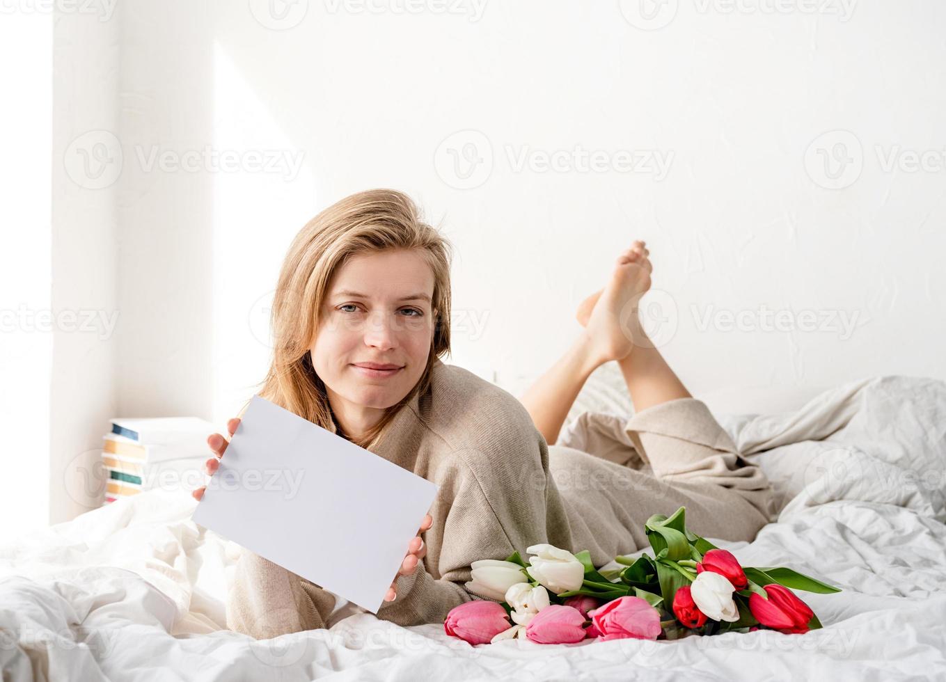 donna sdraiata sul letto in pigiama con in mano un mazzo di fiori di tulipano foto