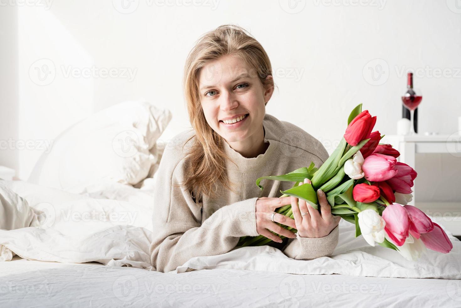 donna sdraiata sul letto in pigiama con in mano un mazzo di fiori di tulipano foto