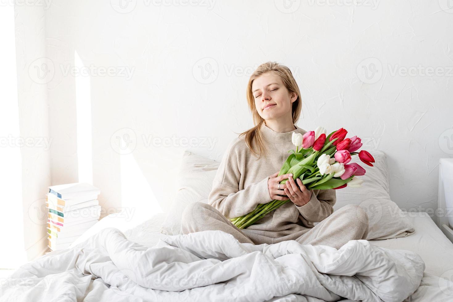 donna seduta sul letto in pigiama con in mano fiori di tulipano foto