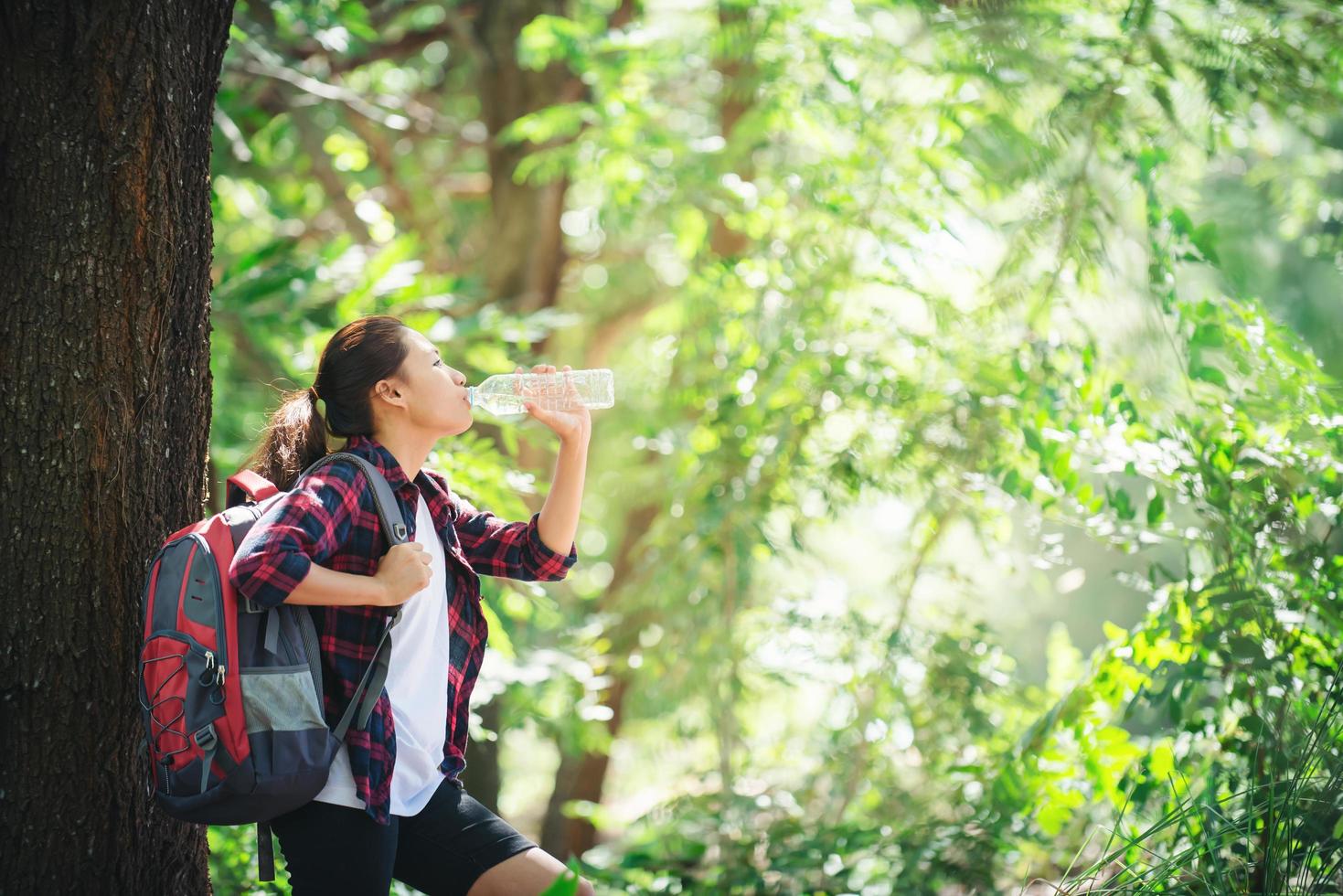 donna che fa una pausa bevendo una bottiglia d'acqua facendo un'escursione nella foresta. foto
