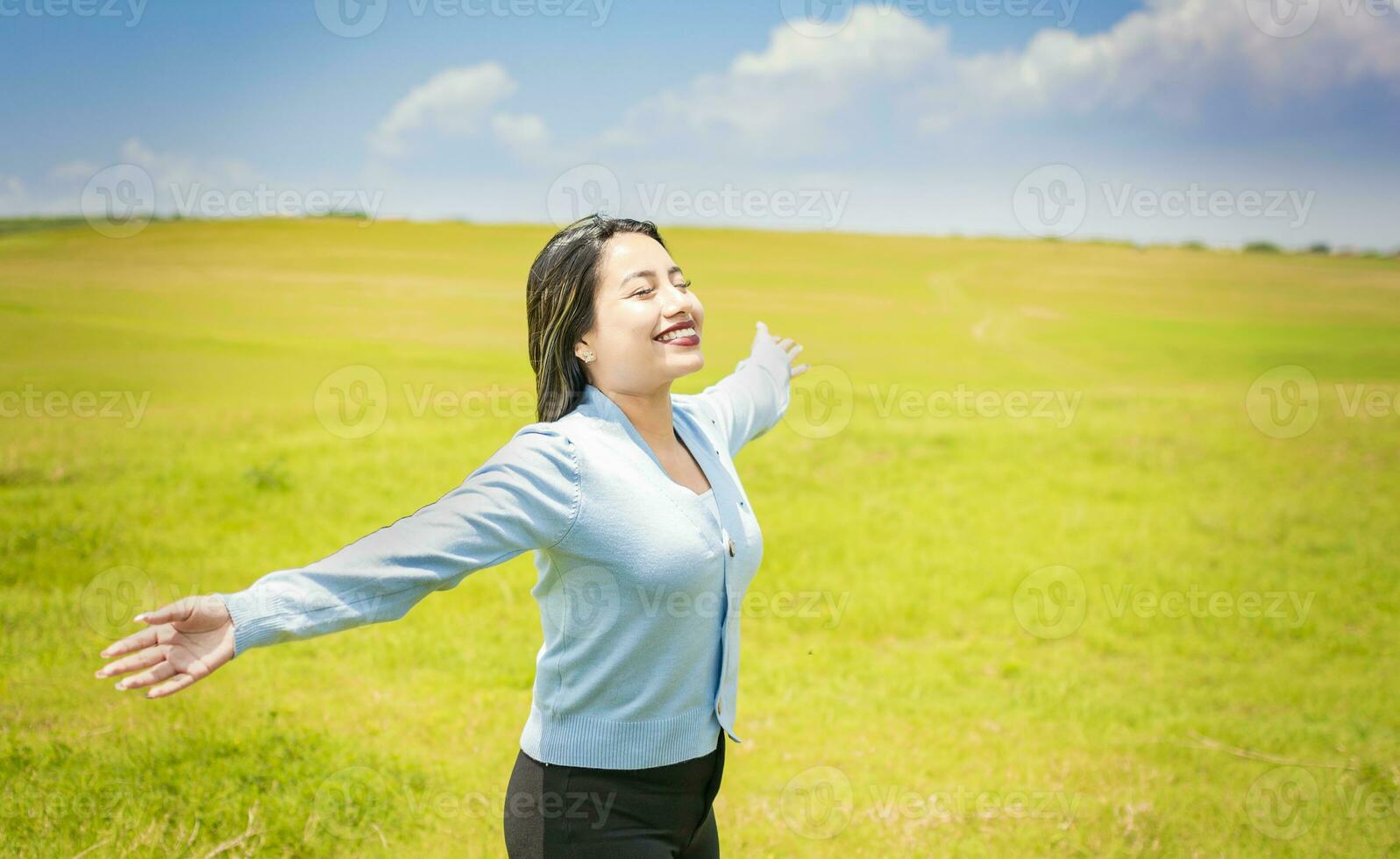 giovane donna sorridente e diffusione sua mani nel il verde campo, concetto di donna respirazione fresco aria nel il campo, contento donna respirazione fresco aria nel il campo e diffusione braccia foto