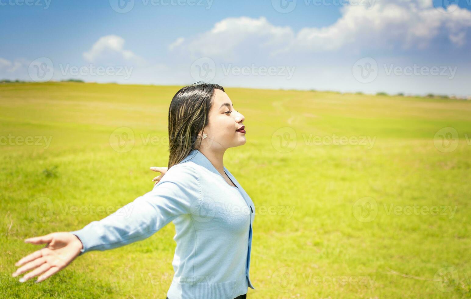 contento donna respirazione fresco aria nel il campo e diffusione braccia, giovane donna sorridente e diffusione sua mani nel il verde campo, concetto di donna respirazione fresco aria nel il campo foto