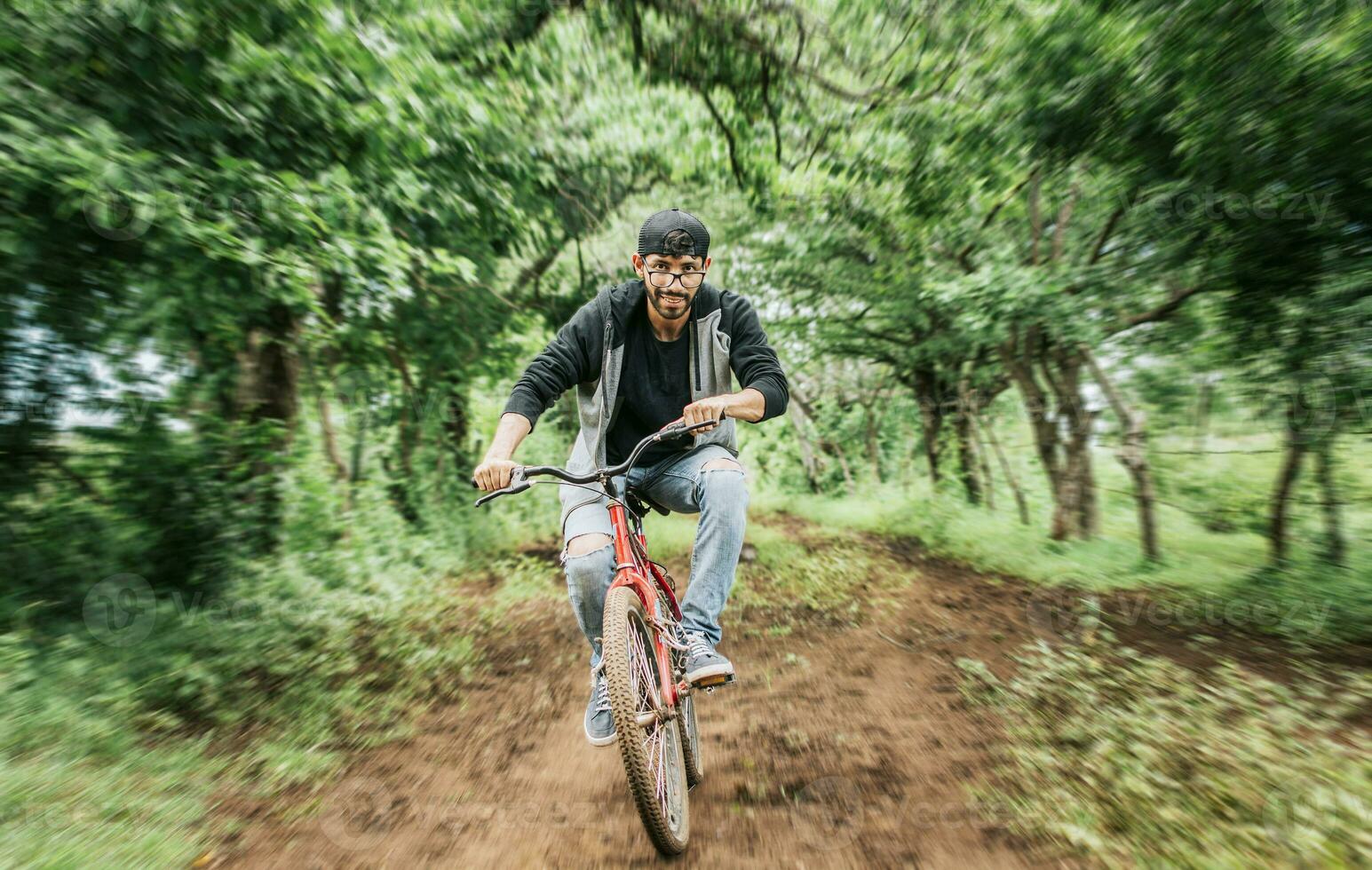 ritratto di un' tipo nel berretto equitazione un' bicicletta su un' nazione strada, persona equitazione un' bicicletta nel il campagna, ciclista persona su il suo bicicletta su un' nazione strada foresta. adolescenziale tipo equitazione un' bicicletta nel il campagna foto