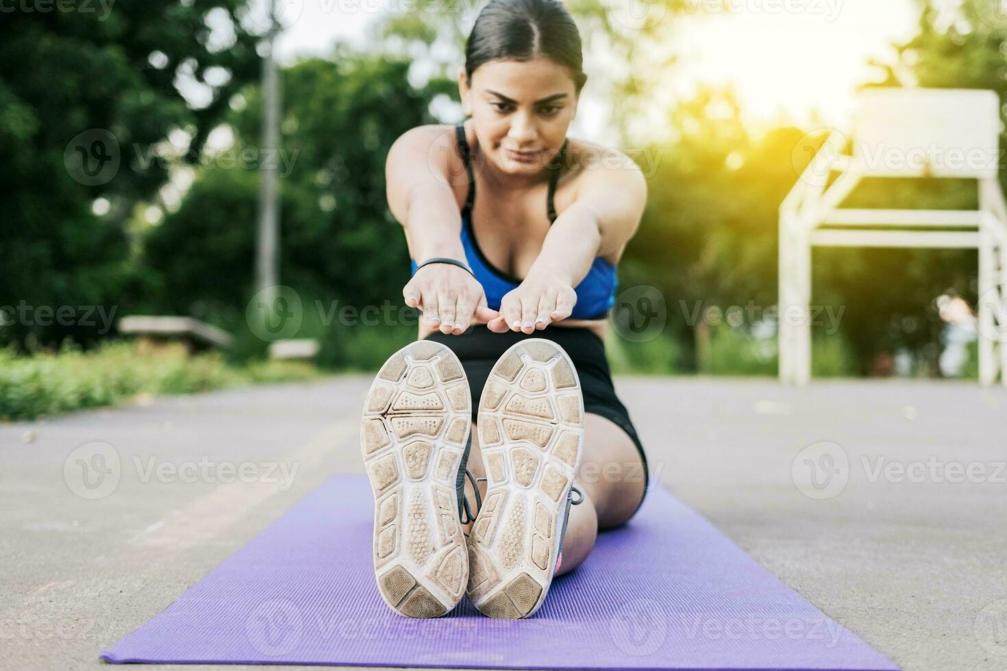 sportivo ragazza allungamento sua gambe seduta su un' stuoia nel un' parco. atleta donna seduta fare gamba allungare nel un' parco. atleta ragazza seduta su un' stuoia allungamento sua gambe nel un' parco foto