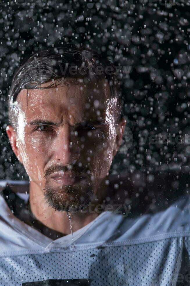 americano calcio campo solitario atleta guerriero in piedi su un' campo detiene il suo casco e pronto per giocare a. giocatore preparazione per correre, attacco e Punto touchdown. piovoso notte con drammatico nebbia, blu leggero foto