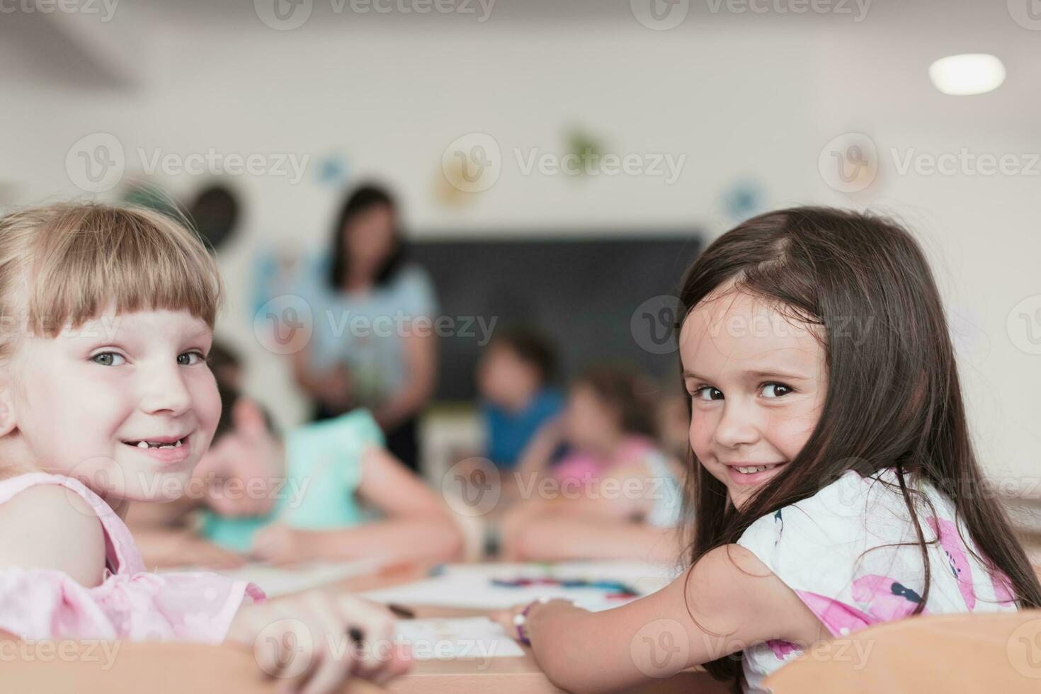 poco ragazze seduta nel elementare scuola disegno su carta con loro amici mentre seduta nel un' moderno aula foto