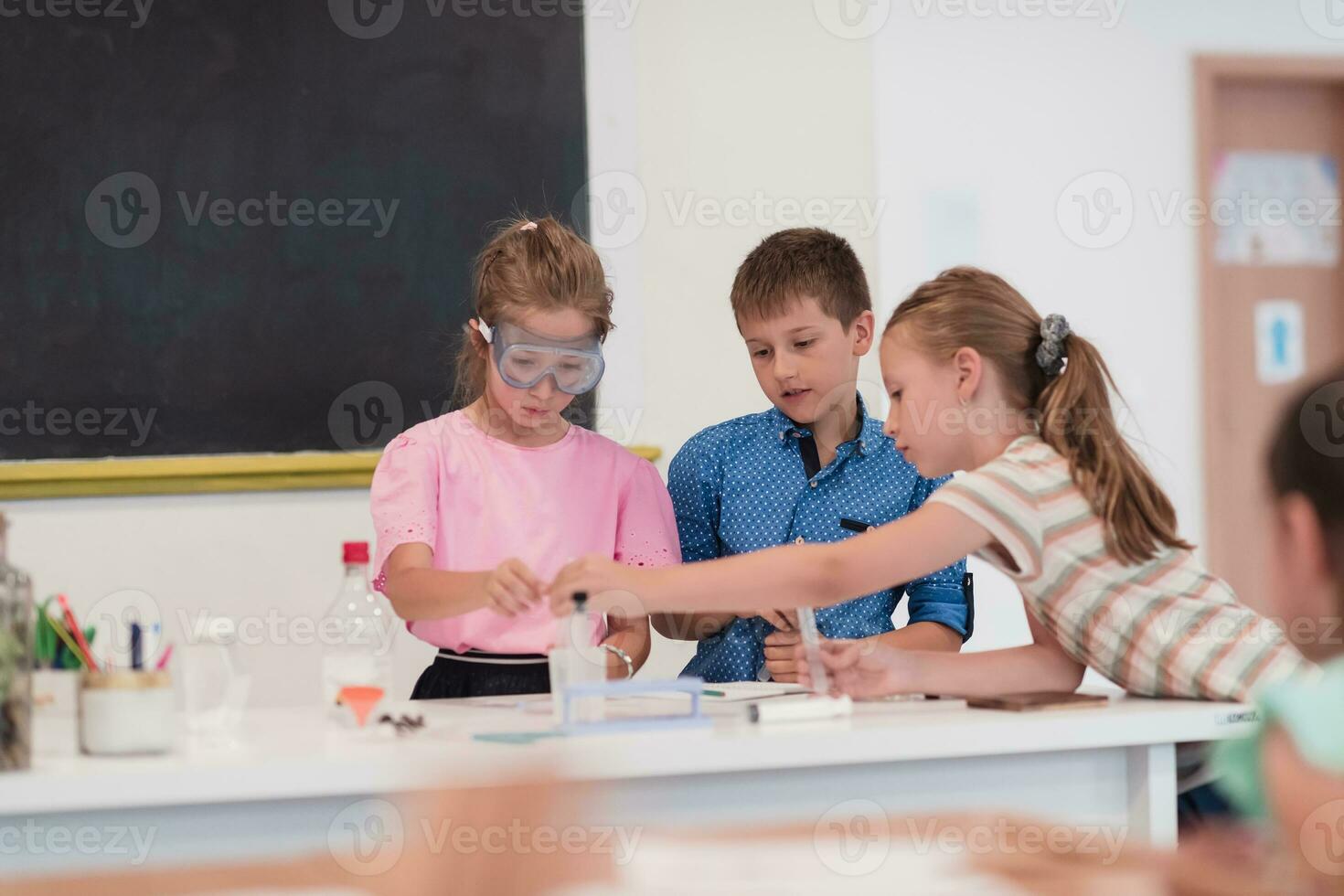 elementare scuola scienza aula entusiasta insegnante spiega chimica per diverso gruppo di figli, poco ragazzo miscele sostanze chimiche nel bicchieri. bambini imparare con interesse foto