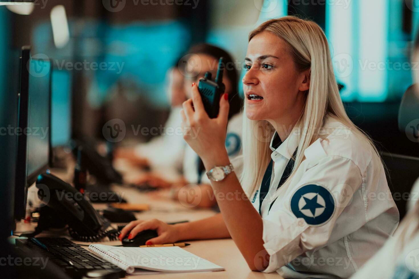 femmina sicurezza operatore Tenere portatile Radio nel mano mentre Lavorando nel un' dati sistema controllo camera uffici tecnico operatore Lavorando a stazione di lavoro con multiplo mostra, sicurezza guardia Lavorando su foto