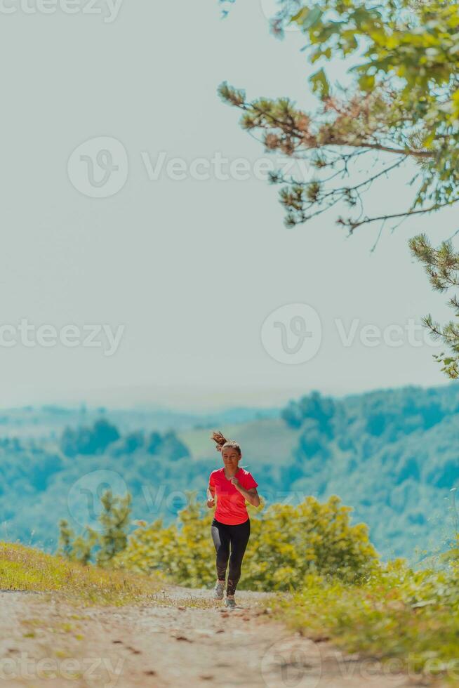 giovane contento donna godendo nel un' salutare stile di vita mentre jogging su un' nazione strada attraverso il bellissimo soleggiato foresta, esercizio e fitness concetto foto