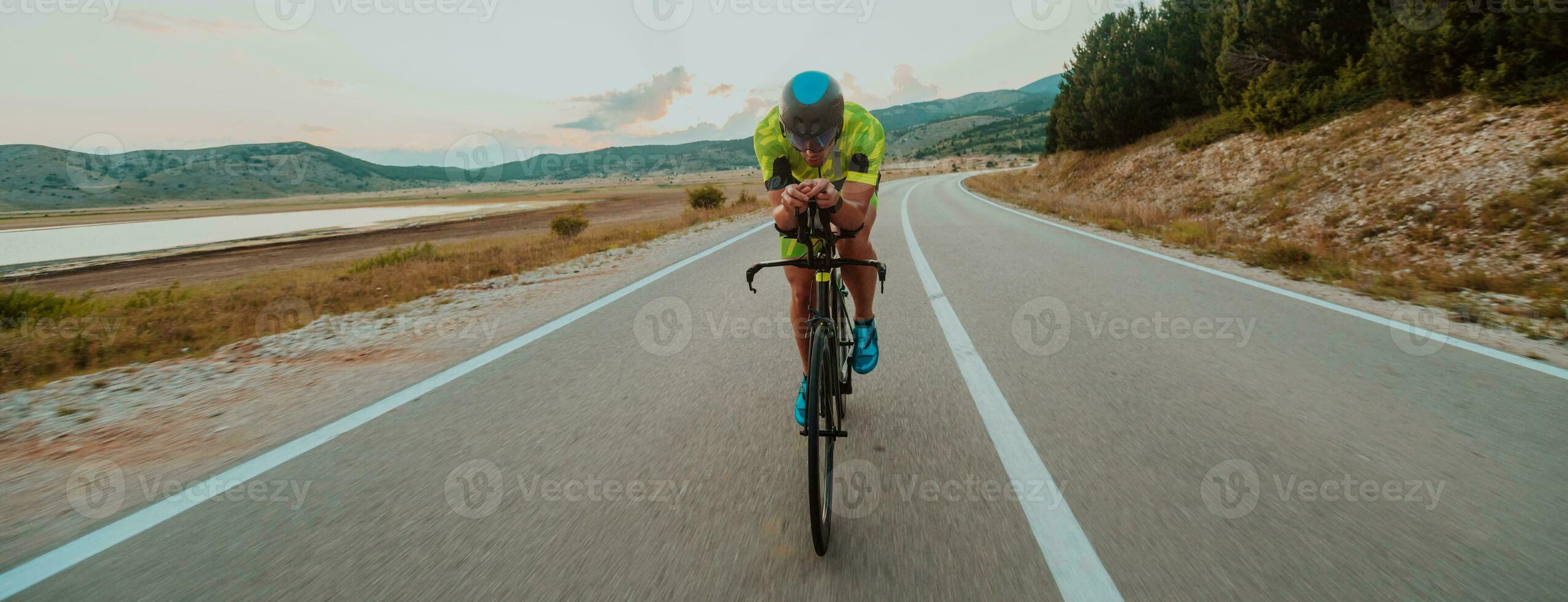 pieno lunghezza ritratto di un attivo triatleta nel abbigliamento sportivo e con un' protettivo casco equitazione un' bicicletta. selettivo messa a fuoco foto